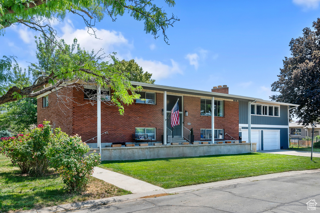 Bi-level home featuring a chimney, a front lawn, driveway, brick siding, and an attached garage