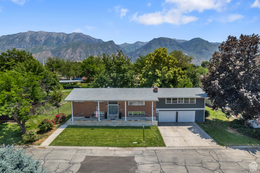View of front of property with an attached garage, concrete driveway, a porch, a chimney, and a mountain view