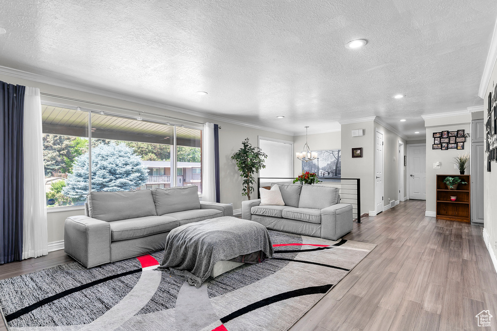 Living area with a chandelier, a textured ceiling, wood finished floors, ornamental molding, and recessed lighting