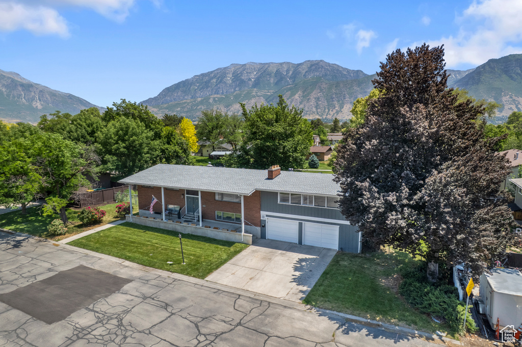 Ranch-style home featuring a mountain view, a front lawn, a chimney, driveway, and a garage