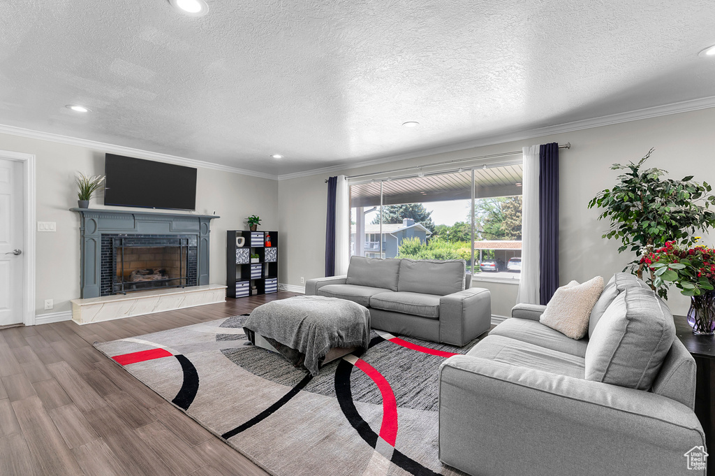 Living room featuring wood finished floors, crown molding, recessed lighting, a fireplace, and a textured ceiling