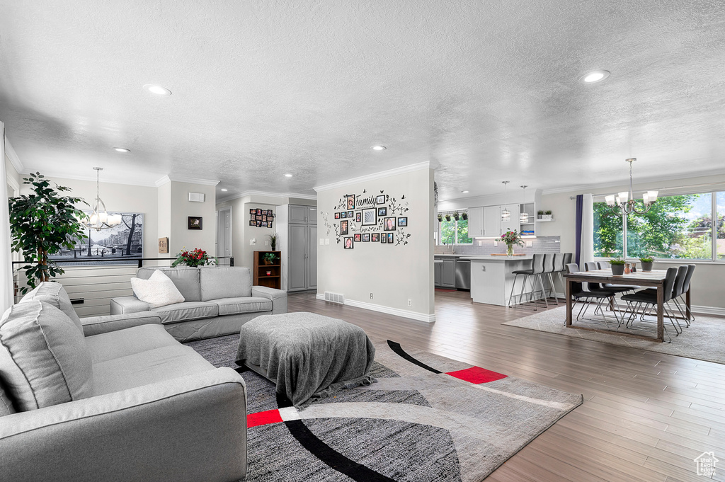 Living room with a chandelier, a textured ceiling, crown molding, recessed lighting, and light wood-style floors