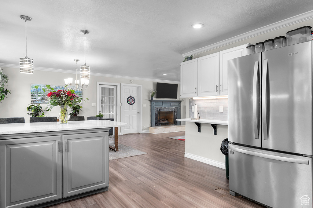 Kitchen with freestanding refrigerator, light countertops, ornamental molding, white cabinetry, and light wood-type flooring