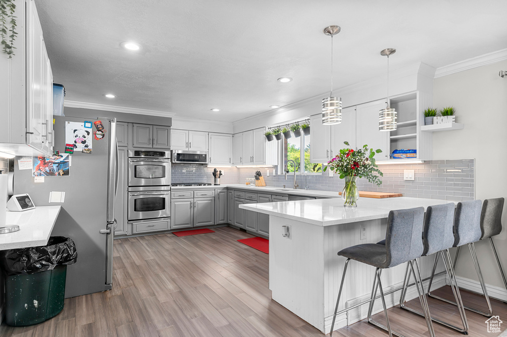 Kitchen featuring appliances with stainless steel finishes, gray cabinets, crown molding, a peninsula, and backsplash