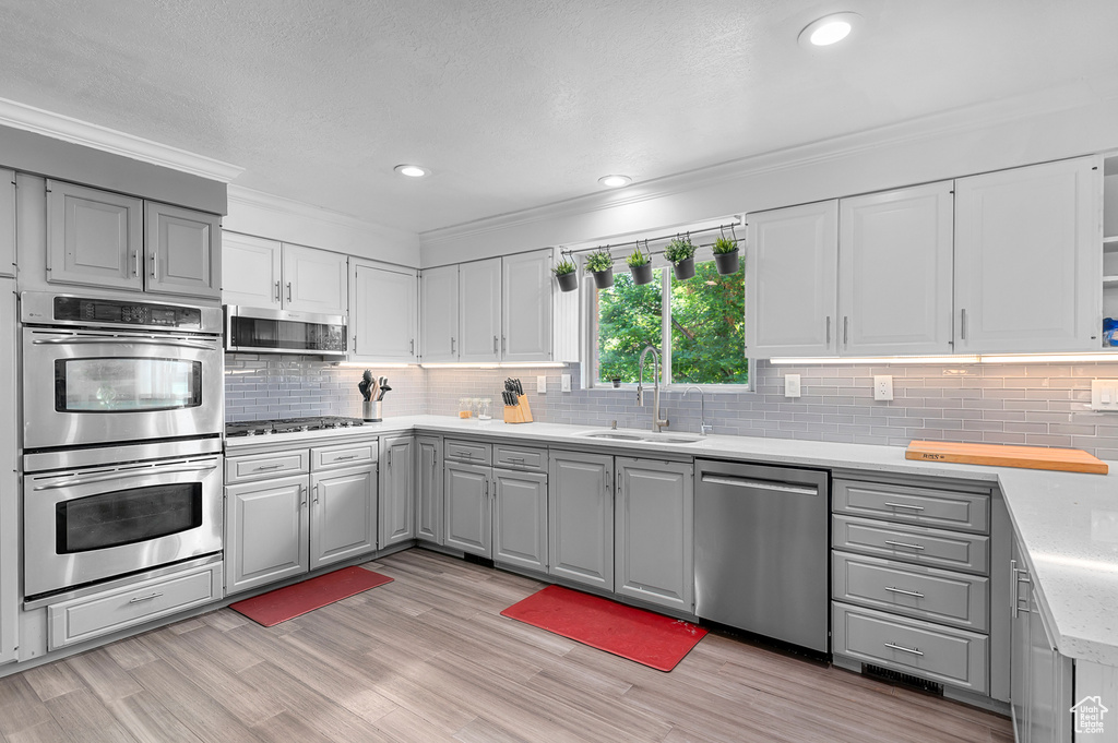 Kitchen featuring appliances with stainless steel finishes, gray cabinets, decorative backsplash, ornamental molding, and light wood-style flooring