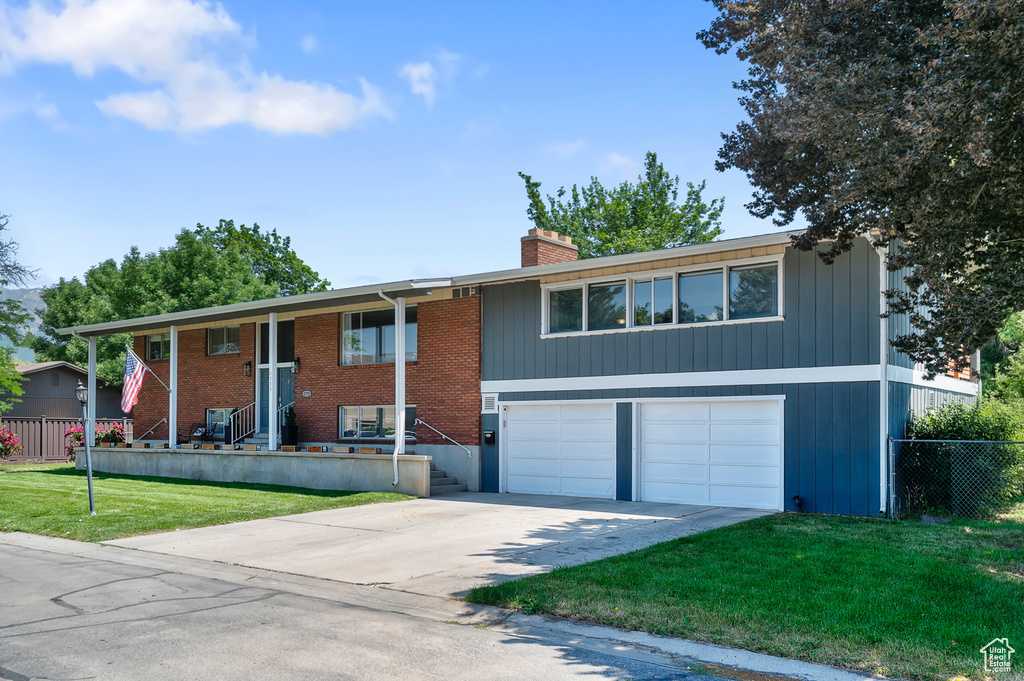 Split foyer home featuring a garage, driveway, a chimney, covered porch, and brick siding