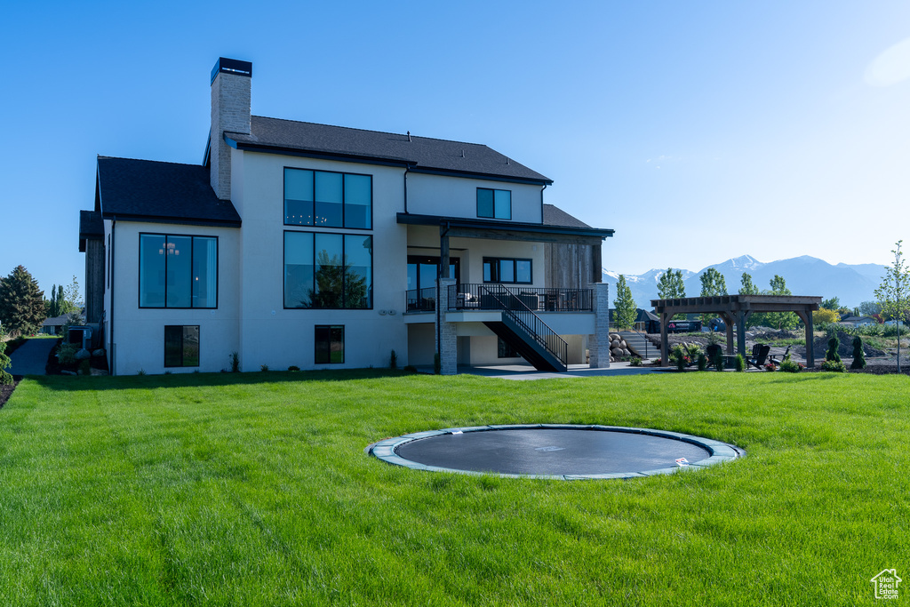 Back of property featuring a trampoline, a yard, stucco siding, a chimney, and a mountain view