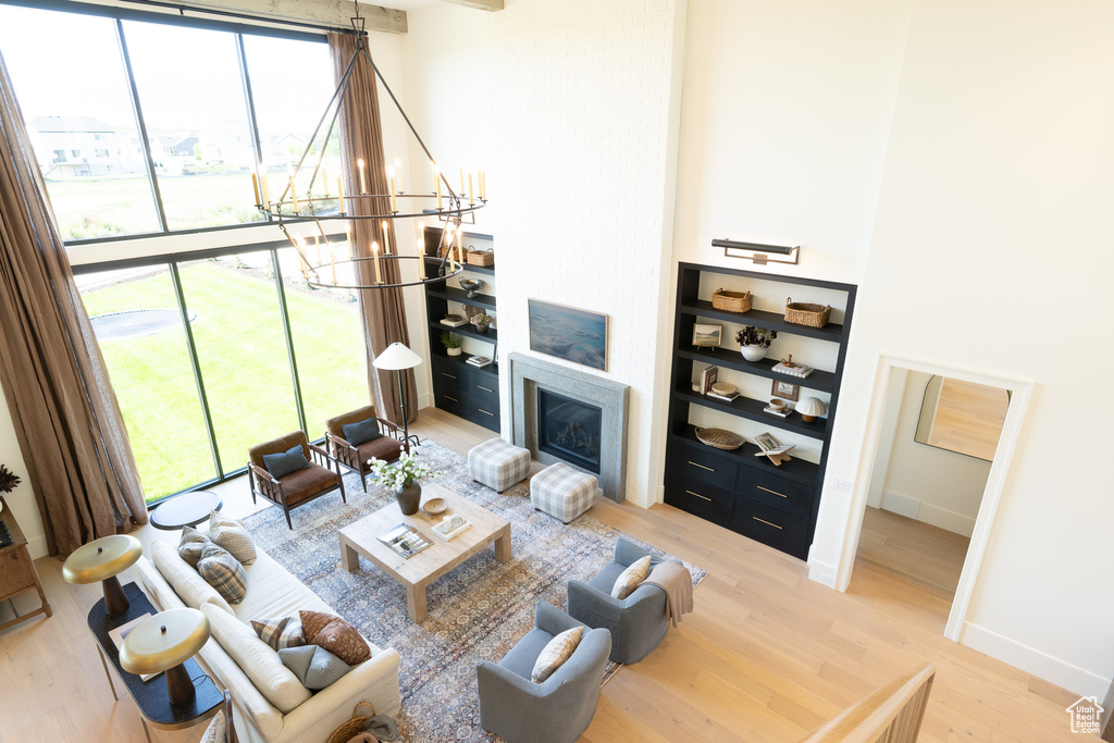 Living room featuring light wood-style flooring, a chandelier, a glass covered fireplace, and built in shelves
