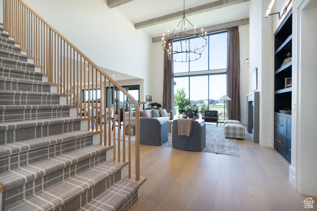 Living area with a chandelier, a towering ceiling, wood-type flooring, stairway, and beamed ceiling