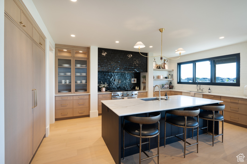 Kitchen featuring backsplash, recessed lighting, a center island with sink, stainless steel range with gas stovetop, and a kitchen breakfast bar