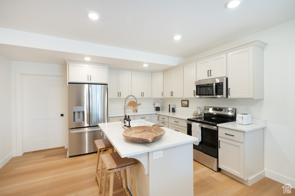 Kitchen with appliances with stainless steel finishes, light wood-type flooring, a center island with sink, a breakfast bar area, and light countertops