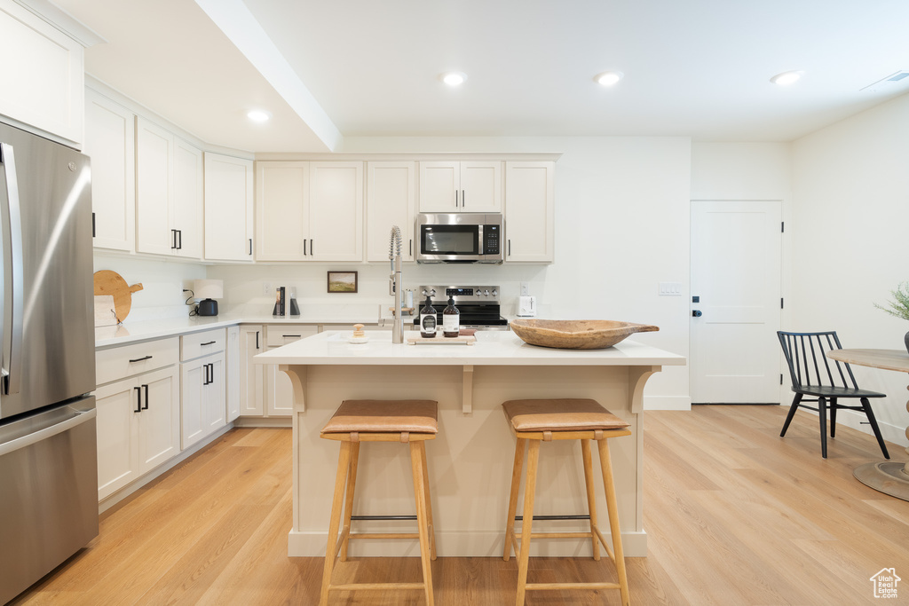 Kitchen featuring appliances with stainless steel finishes, a kitchen breakfast bar, light countertops, light wood-style floors, and recessed lighting