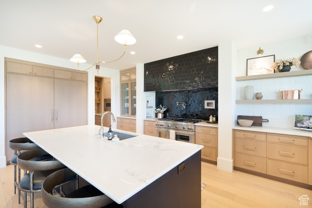 Kitchen featuring high end stainless steel range oven, decorative backsplash, light wood-style flooring, light brown cabinetry, and a kitchen bar