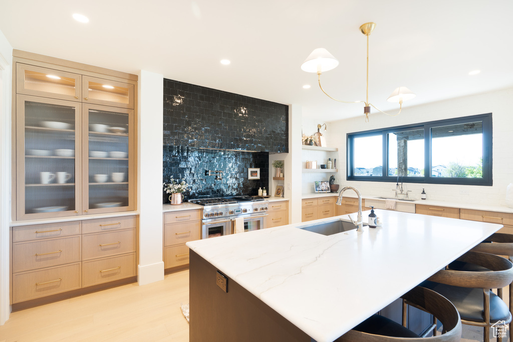 Kitchen featuring range with two ovens, recessed lighting, decorative backsplash, a breakfast bar area, and a kitchen island with sink