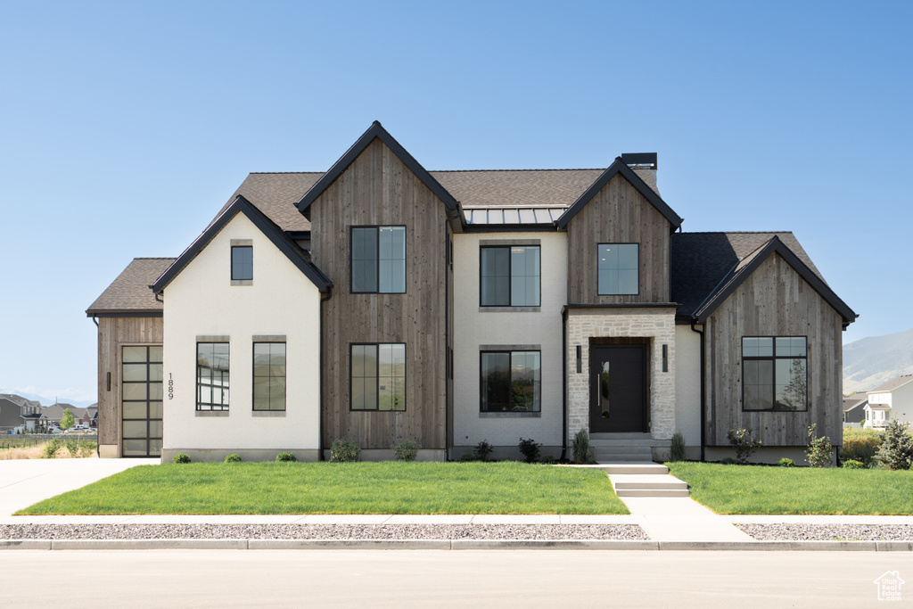 Modern farmhouse with a front yard, a chimney, and concrete driveway