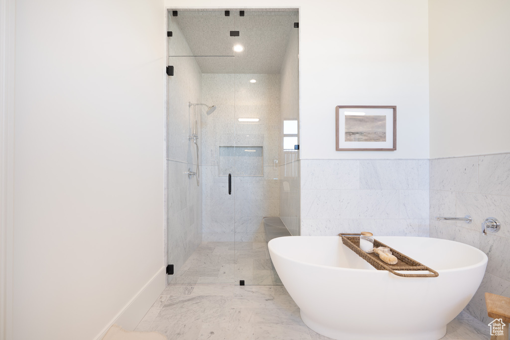 Bathroom featuring a shower stall, a soaking tub, and tile walls
