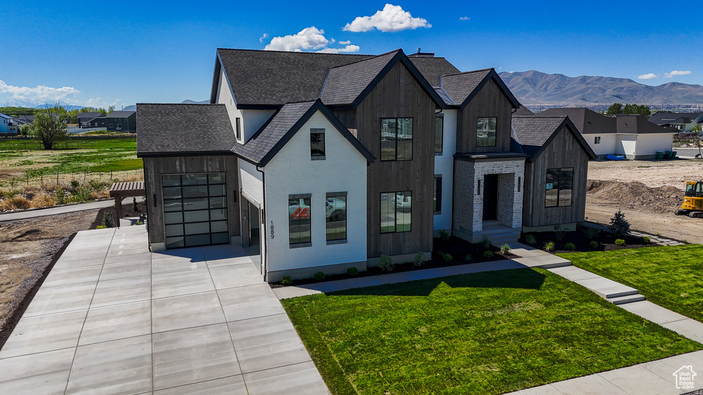 View of front of house featuring a shingled roof, a front lawn, a mountain view, and concrete driveway