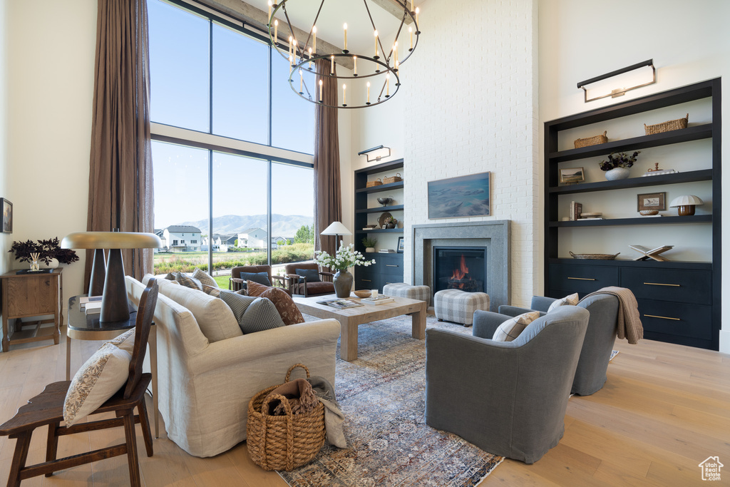 Living area featuring a high ceiling, light wood finished floors, a chandelier, a warm lit fireplace, and a mountain view