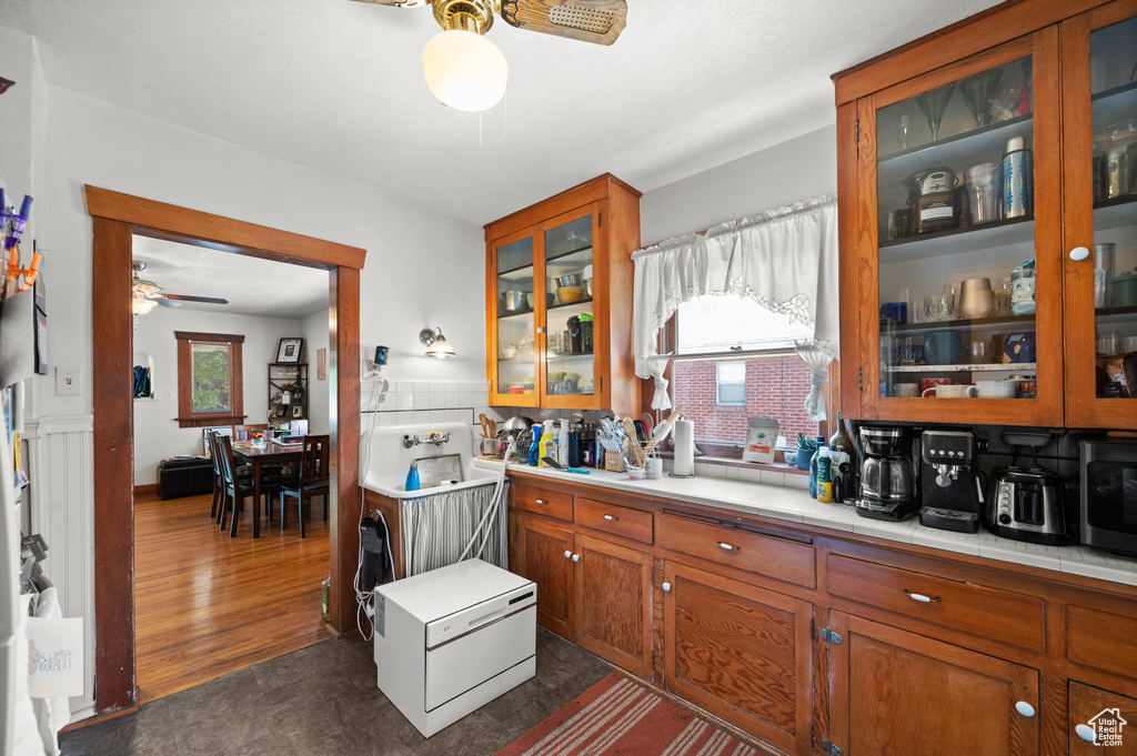 Kitchen featuring ceiling fan, brown cabinets, glass insert cabinets, and tile counters
