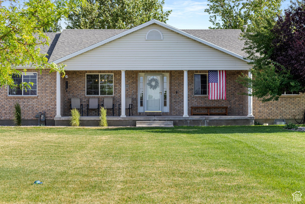 View of front of property with a porch, brick siding, a front yard, and roof with shingles