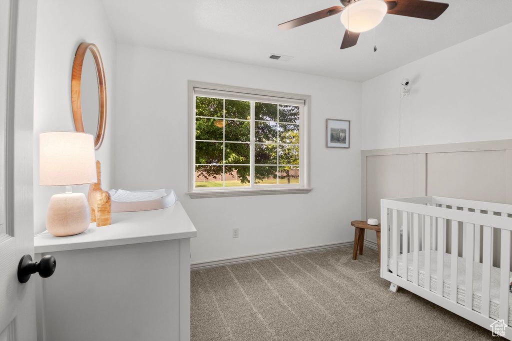 Carpeted bedroom with a nursery area, ceiling fan, and wainscoting