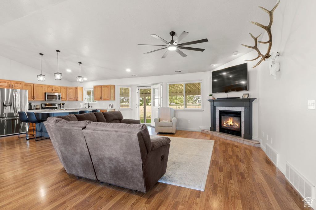 Living area with vaulted ceiling, ceiling fan, a tiled fireplace, wood finished floors, and recessed lighting