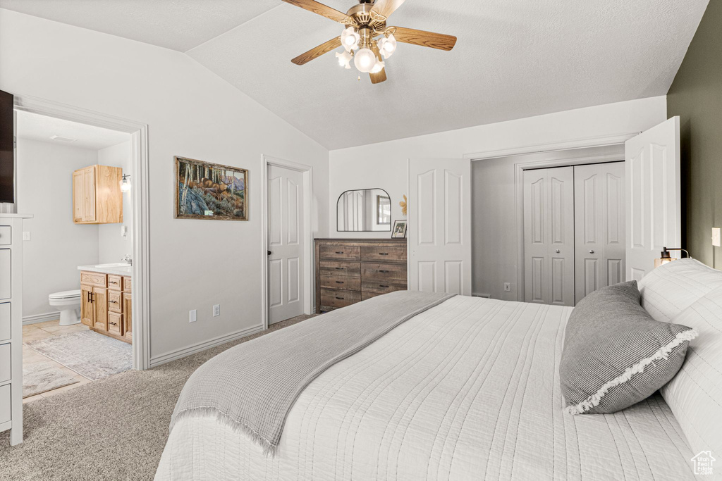 Bedroom with lofted ceiling, light carpet, a closet, ceiling fan, and ensuite bath