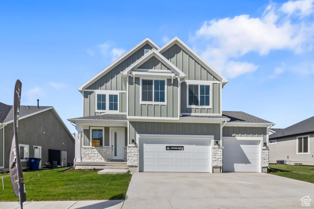 Craftsman house with board and batten siding, stone siding, a front yard, and driveway
