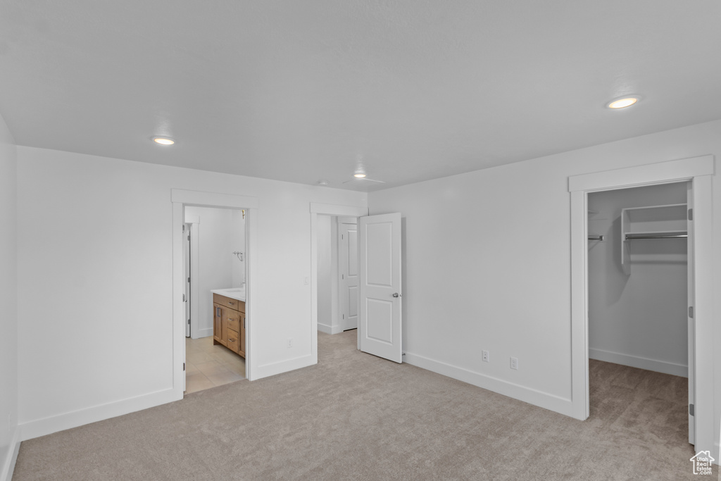 Unfurnished bedroom with light colored carpet, a walk in closet, recessed lighting, a closet, and connected bathroom
