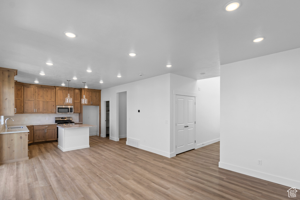 Kitchen with appliances with stainless steel finishes, recessed lighting, light countertops, light wood-type flooring, and a center island
