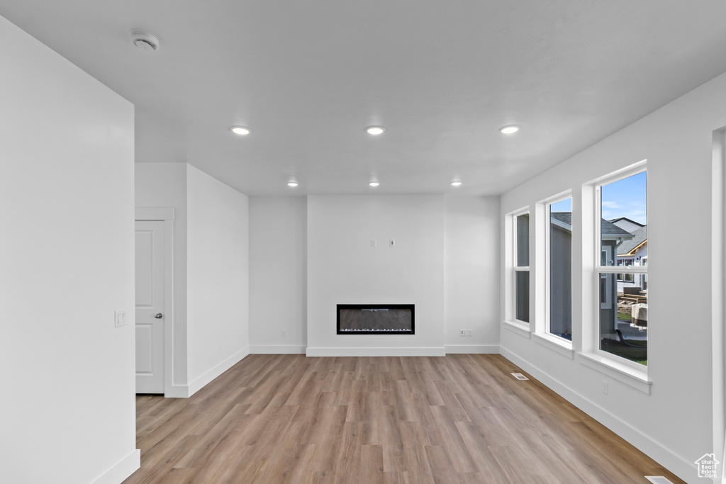 Unfurnished living room featuring light wood-style floors, a glass covered fireplace, and recessed lighting