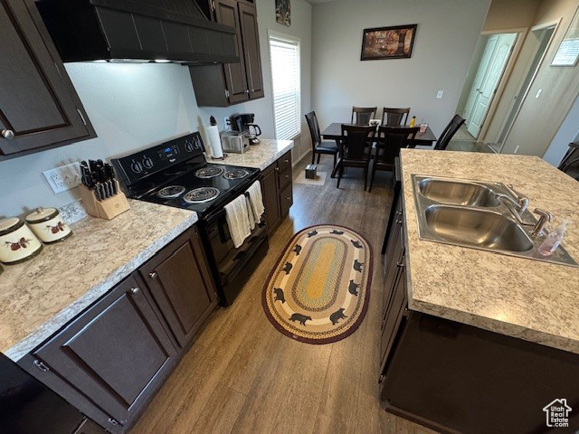 Kitchen featuring black electric range oven, wall chimney range hood, dark wood-style flooring, and light countertops