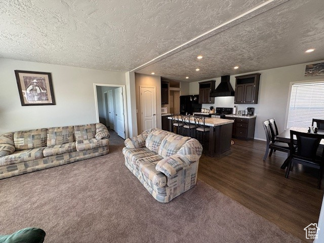 Living room with a textured ceiling, recessed lighting, dark wood-type flooring, and dark carpet