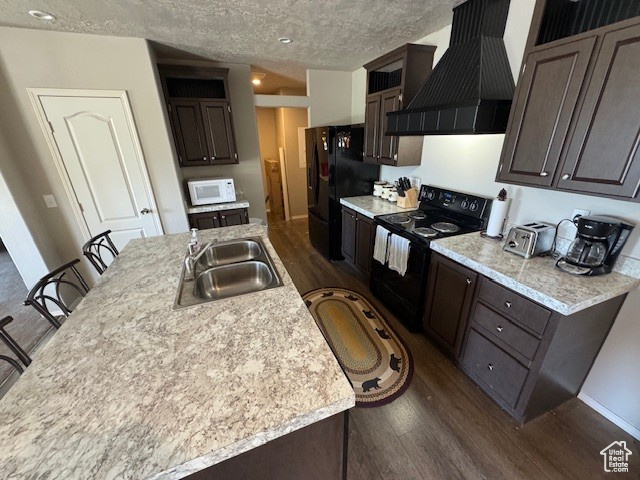 Kitchen featuring black appliances, custom range hood, dark wood-style floors, light countertops, and a textured ceiling
