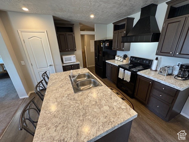 Kitchen featuring black appliances, custom exhaust hood, a kitchen island with sink, light countertops, and a textured ceiling