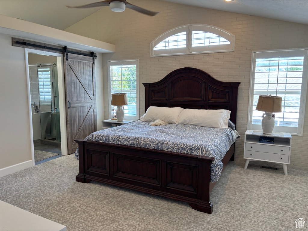 Bedroom with vaulted ceiling, light colored carpet, a barn door, a ceiling fan, and brick wall