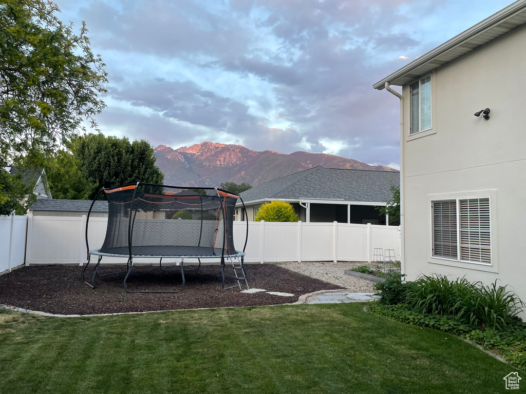 Fenced backyard featuring a trampoline and a mountain view