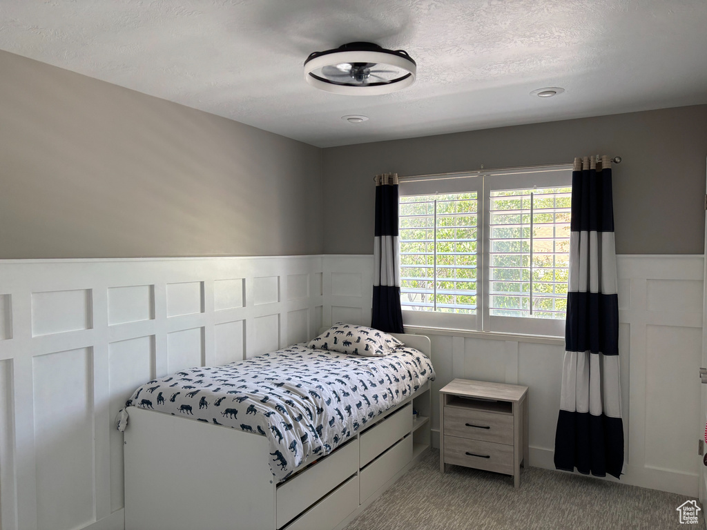 Bedroom with a decorative wall, light carpet, a wainscoted wall, and a textured ceiling