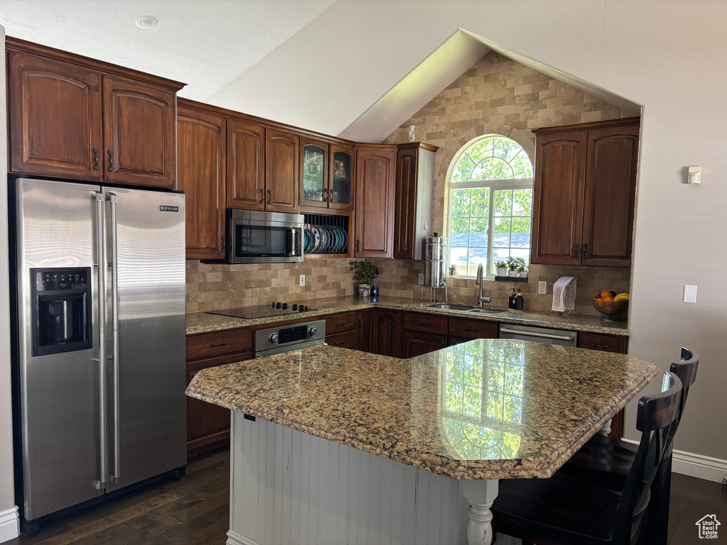 Kitchen with stainless steel appliances, vaulted ceiling, dark wood finished floors, light stone countertops, and backsplash