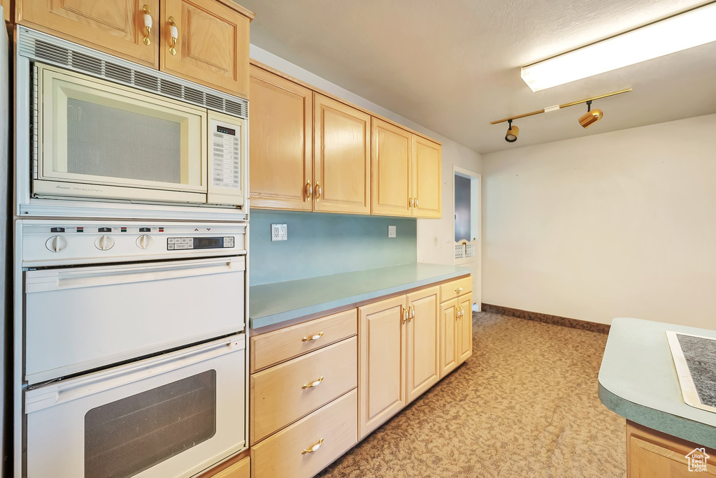 Kitchen with white appliances, light brown cabinetry, and light countertops
