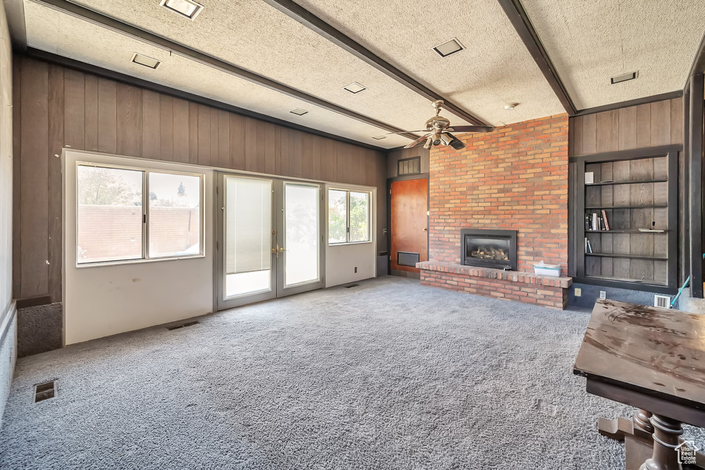 Unfurnished living room featuring wood walls, ceiling fan, french doors, a brick fireplace, and beamed ceiling