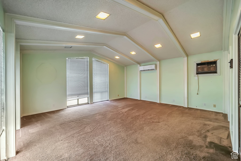 Empty room featuring carpet, a wall unit AC, and lofted ceiling