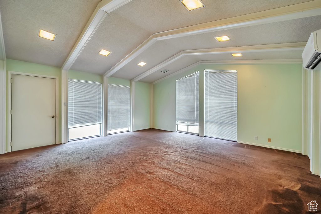 Unfurnished living room featuring carpet flooring, lofted ceiling, a textured ceiling, and an AC wall unit