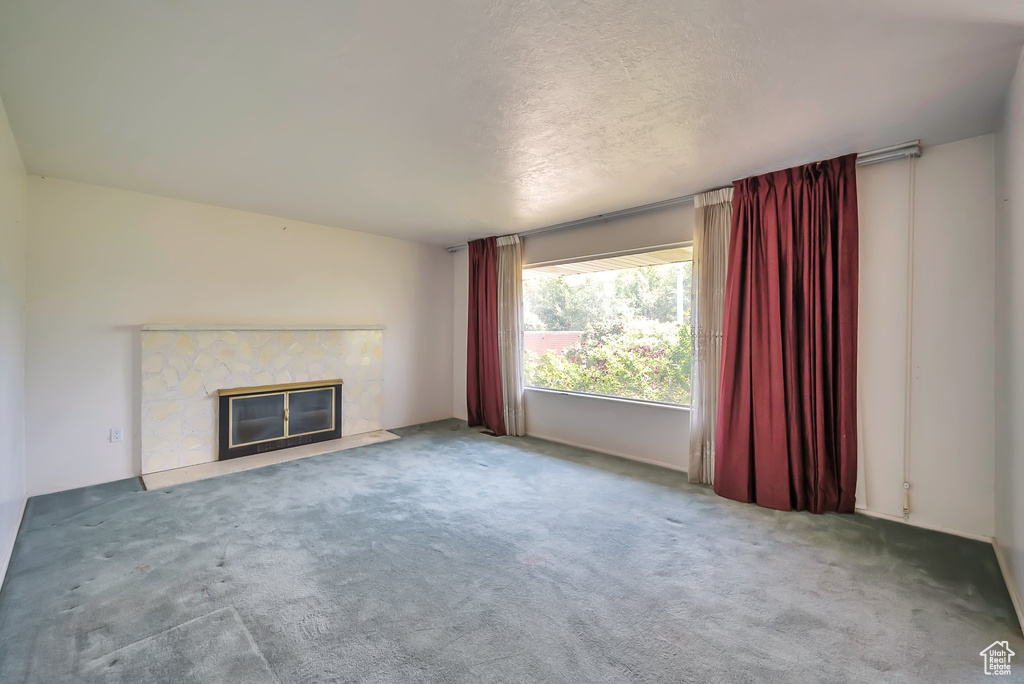 Unfurnished living room featuring a high end fireplace, carpet, and a textured ceiling