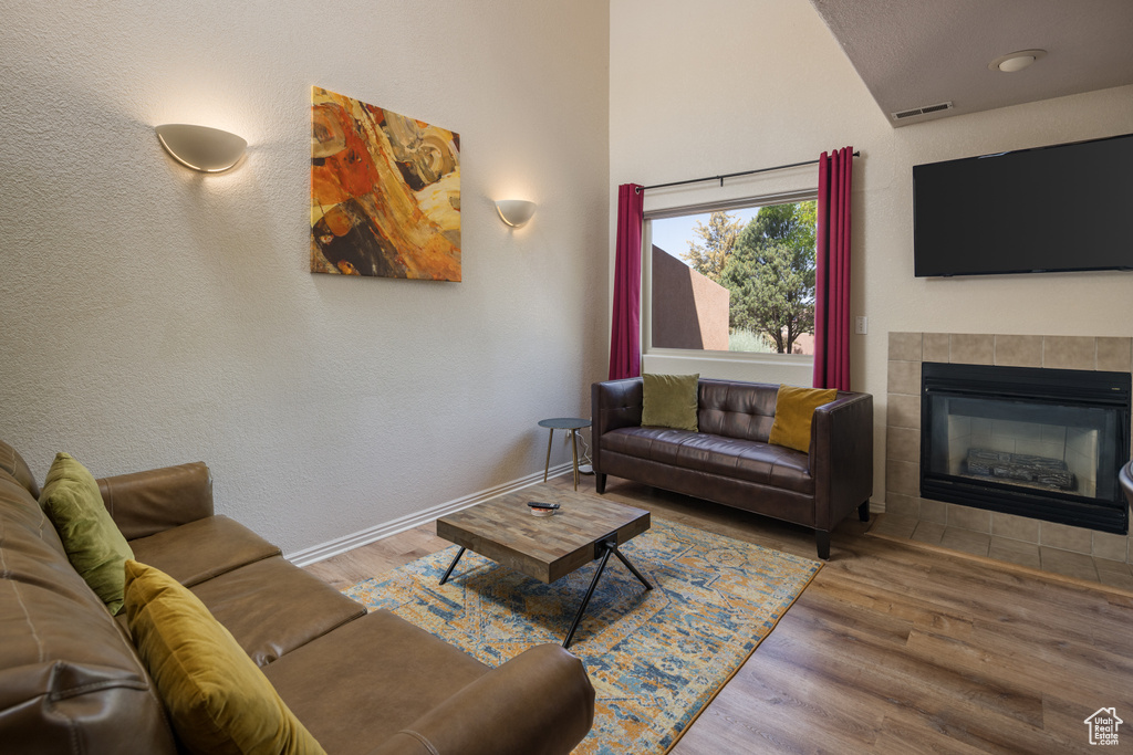 Living room featuring a tile fireplace, wood finished floors, and lofted ceiling
