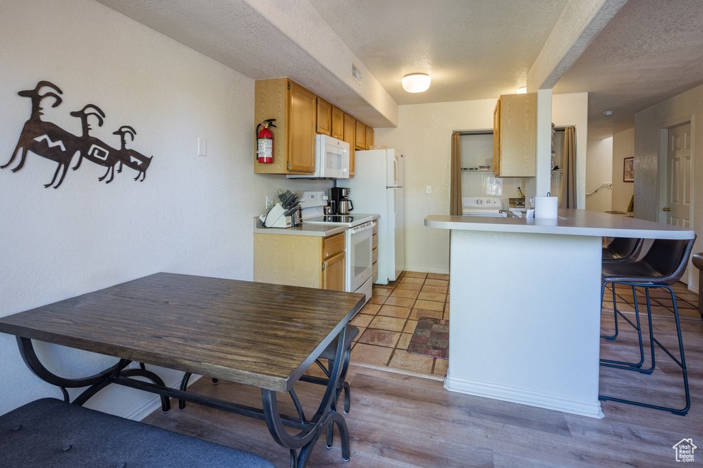 Kitchen with white appliances, a breakfast bar, a peninsula, light countertops, and washer / clothes dryer
