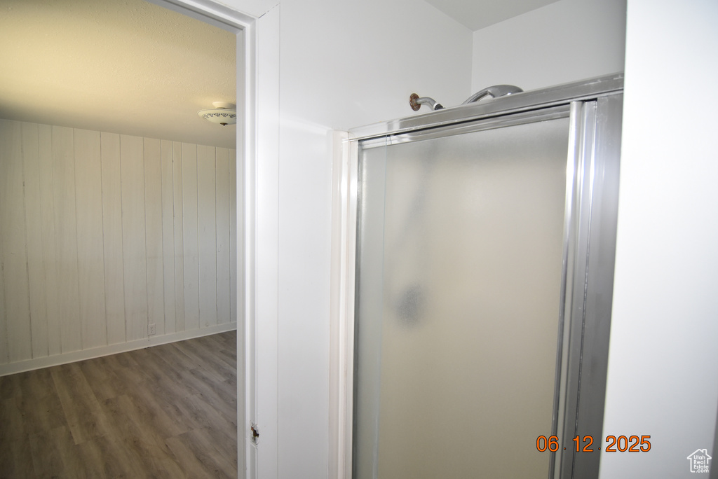 Bathroom featuring wood finished floors, a shower with shower door, and wood walls