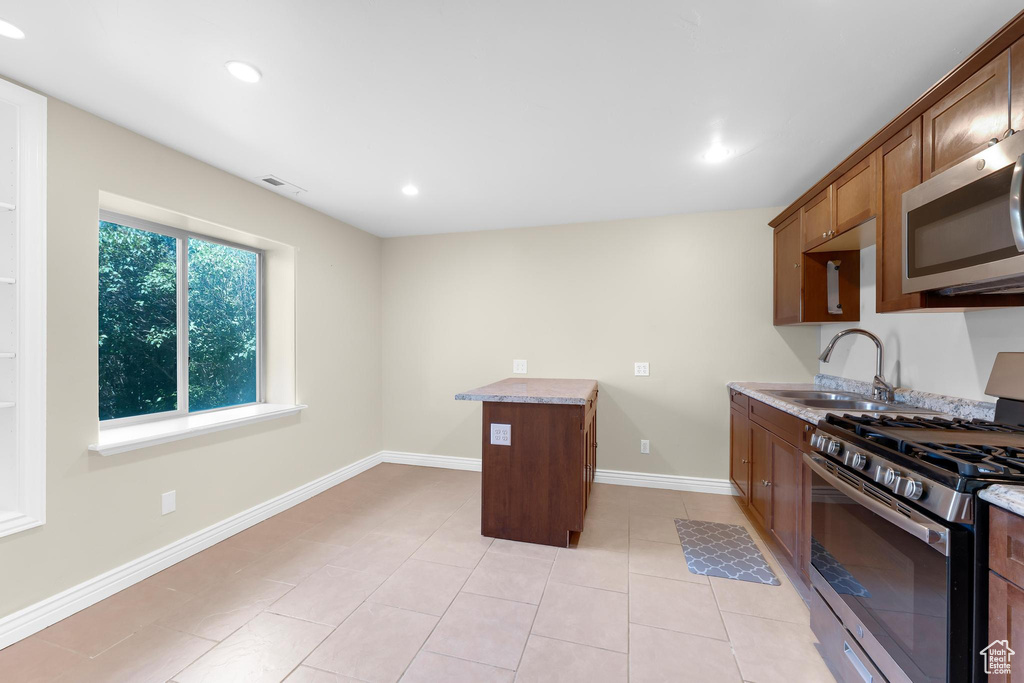 Kitchen with appliances with stainless steel finishes, light tile patterned flooring, recessed lighting, light stone counters, and brown cabinetry