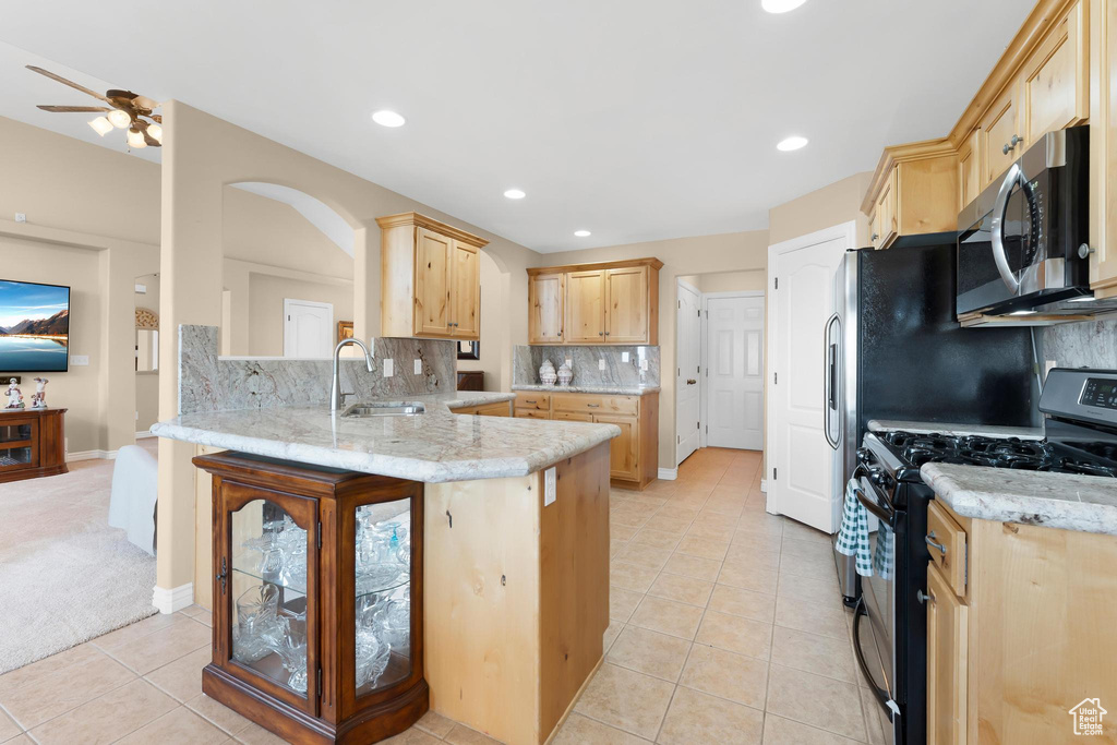 Kitchen with stainless steel microwave, gas stove, light brown cabinetry, a peninsula, and light tile patterned floors