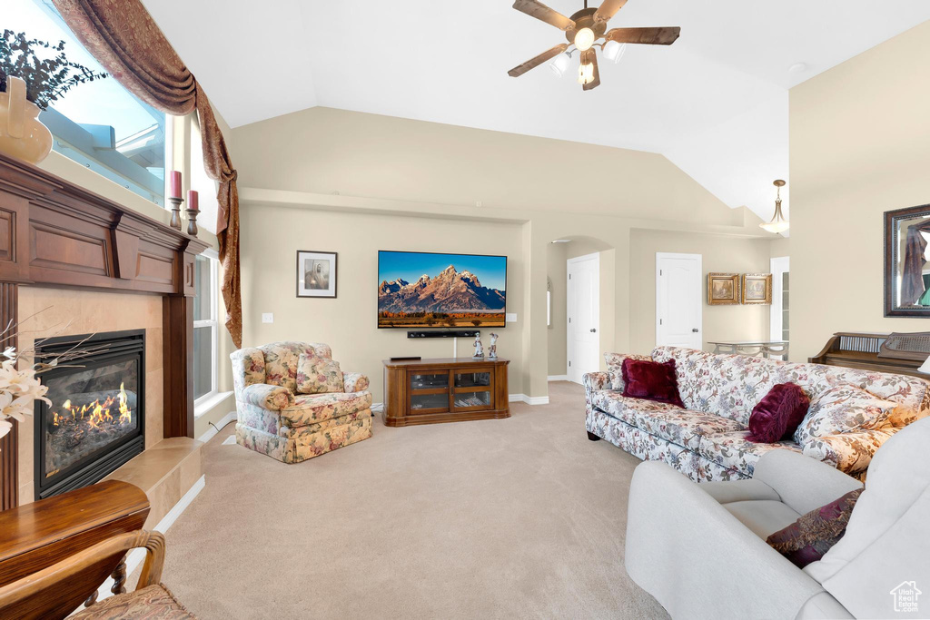 Living room featuring lofted ceiling, arched walkways, a fireplace, light carpet, and a ceiling fan